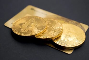 Three gold bitcoins laying on top of a gold credit card.