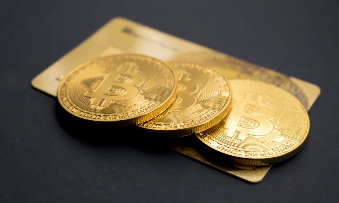 Three gold bitcoins laying on top of a gold credit card.